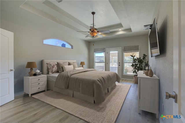 bedroom featuring ceiling fan, access to exterior, a raised ceiling, and hardwood / wood-style floors