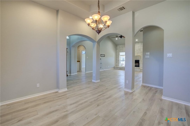 unfurnished dining area featuring a stone fireplace, ceiling fan with notable chandelier, light hardwood / wood-style flooring, and a high ceiling