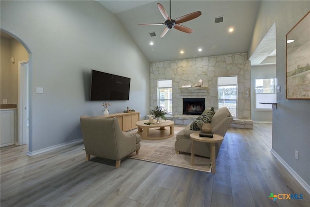 living room with high vaulted ceiling, a stone fireplace, a wealth of natural light, and light wood-type flooring