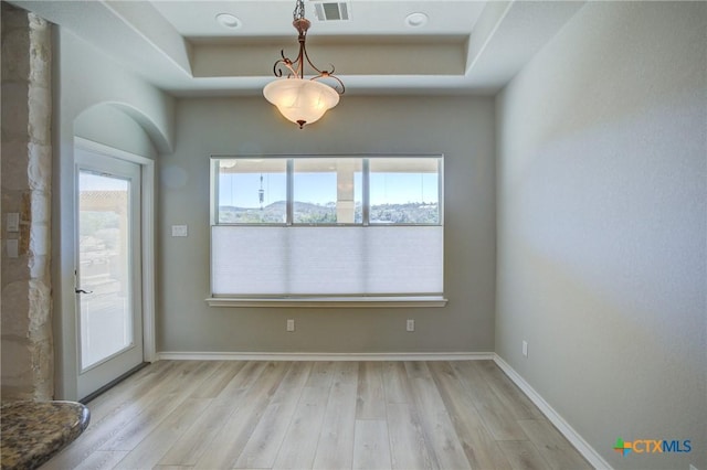 unfurnished dining area with a raised ceiling and light hardwood / wood-style flooring