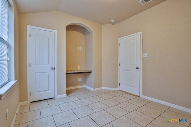 unfurnished room with light tile patterned floors and vaulted ceiling