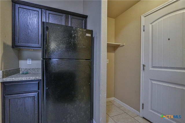 kitchen with black refrigerator, light stone countertops, and light tile patterned floors