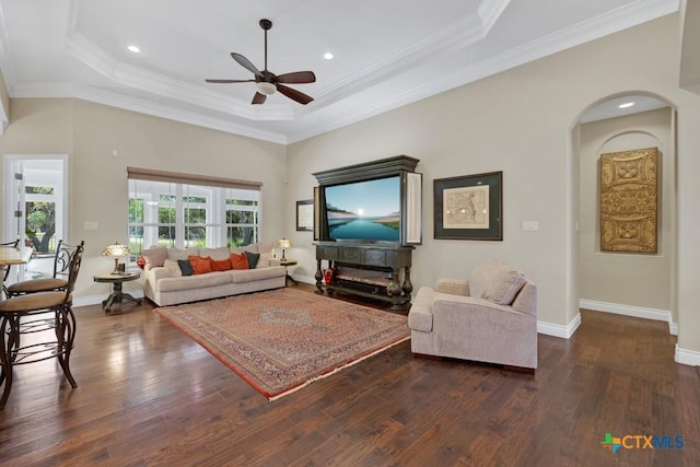living room with dark wood-style flooring, ceiling fan, a raised ceiling, baseboards, and ornamental molding