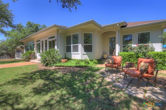 rear view of house featuring a lawn, fence, and stucco siding