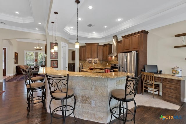 kitchen featuring dark wood-style flooring, appliances with stainless steel finishes, a raised ceiling, wall chimney exhaust hood, and visible vents