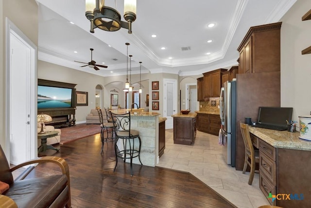 kitchen featuring a breakfast bar area, arched walkways, freestanding refrigerator, open floor plan, and a tray ceiling