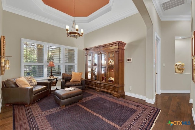 living area featuring a chandelier, baseboards, wood finished floors, visible vents, and ornamental molding