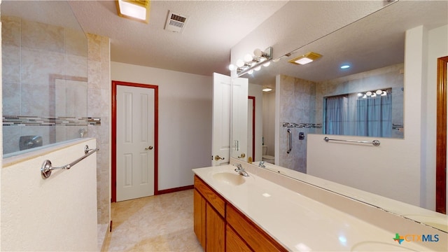 bathroom with vanity, a textured ceiling, toilet, and a tile shower