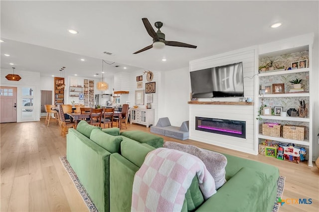 living room featuring ceiling fan, light wood-type flooring, and a fireplace