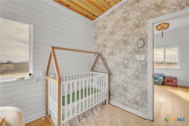 bedroom featuring wood ceiling, a crib, multiple windows, and hardwood / wood-style flooring