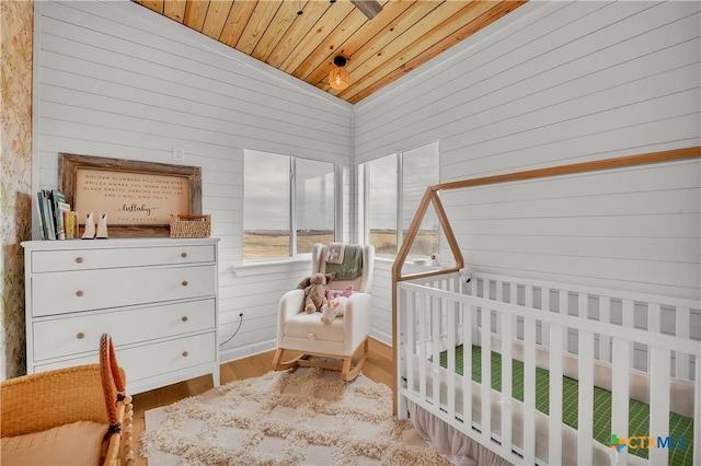 bedroom with lofted ceiling, wood ceiling, wooden walls, and light hardwood / wood-style floors