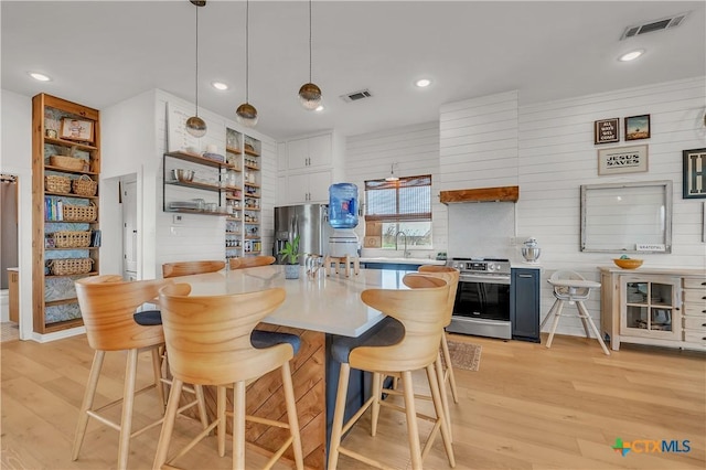 kitchen with white cabinets, hanging light fixtures, appliances with stainless steel finishes, and a breakfast bar