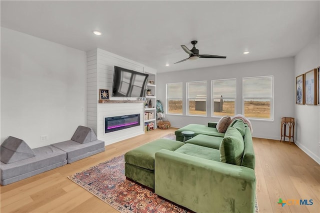 living room featuring ceiling fan, a large fireplace, and hardwood / wood-style flooring