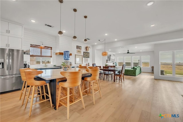 kitchen featuring ceiling fan, pendant lighting, a kitchen bar, stainless steel refrigerator with ice dispenser, and white cabinetry