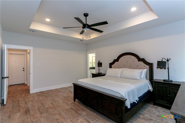 bedroom with light wood-type flooring, ceiling fan, and a raised ceiling