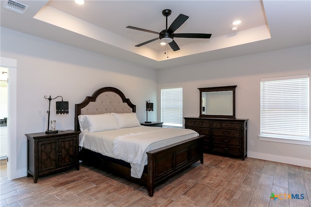 bedroom with hardwood / wood-style floors, ceiling fan, and a tray ceiling