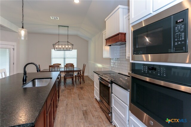 kitchen featuring white cabinetry, sink, appliances with stainless steel finishes, hanging light fixtures, and lofted ceiling