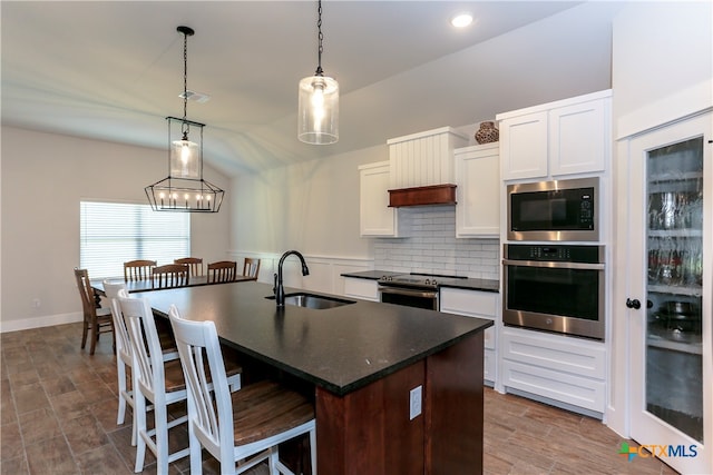 kitchen with stainless steel appliances, sink, a kitchen island with sink, white cabinets, and pendant lighting