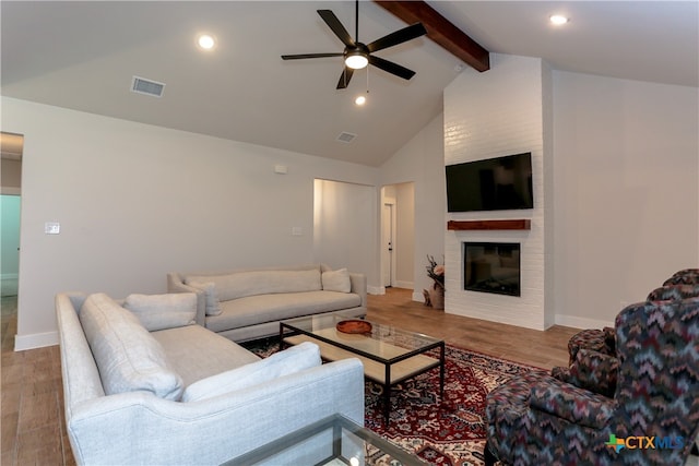 living room featuring beamed ceiling, hardwood / wood-style flooring, ceiling fan, and a brick fireplace