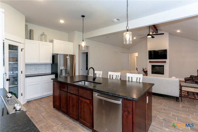 kitchen with stainless steel appliances, a center island with sink, sink, a large fireplace, and lofted ceiling with beams