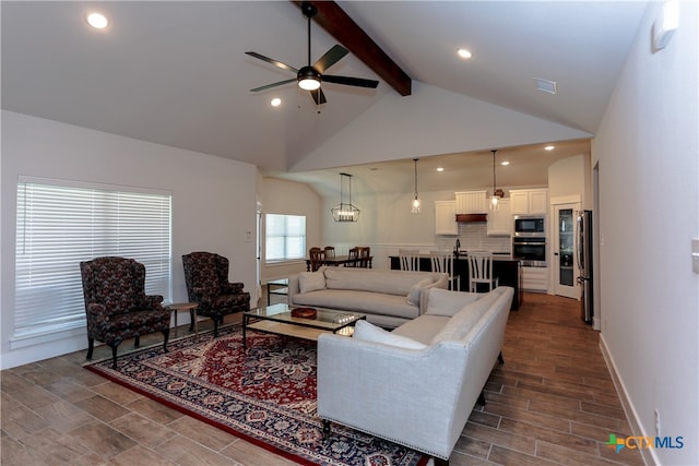 living room featuring dark wood-type flooring, ceiling fan with notable chandelier, beam ceiling, and high vaulted ceiling