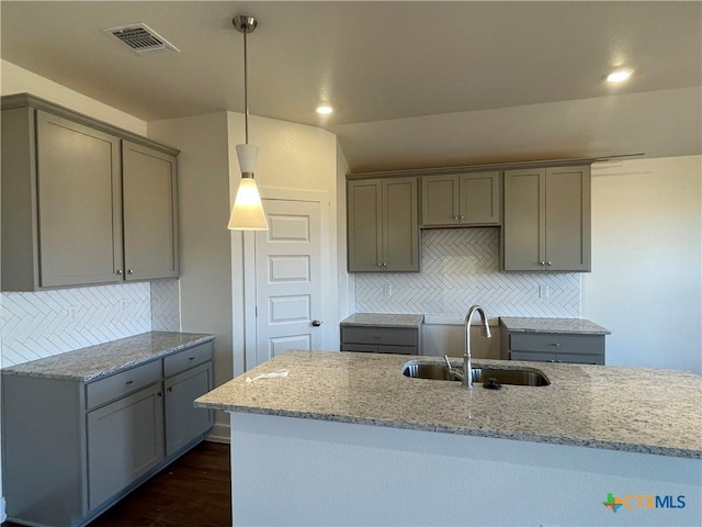 kitchen with pendant lighting, backsplash, light stone countertops, and sink