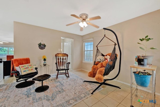 living area featuring light tile patterned floors, baseboards, and a ceiling fan