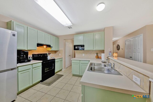 kitchen with a peninsula, a sink, backsplash, black appliances, and green cabinets