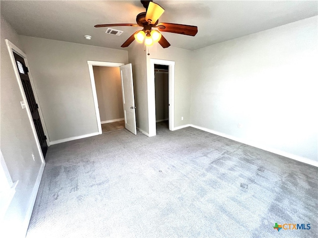 unfurnished bedroom featuring a walk in closet, carpet floors, a closet, and ceiling fan