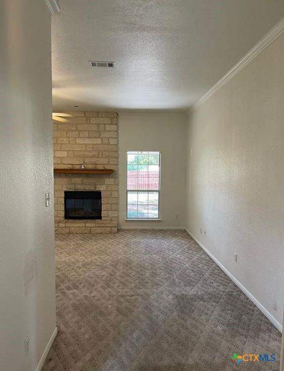 unfurnished living room with a brick fireplace, carpet floors, ornamental molding, and a textured ceiling