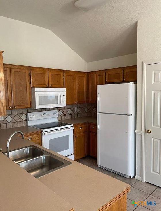 kitchen with light tile patterned floors, white appliances, sink, backsplash, and vaulted ceiling