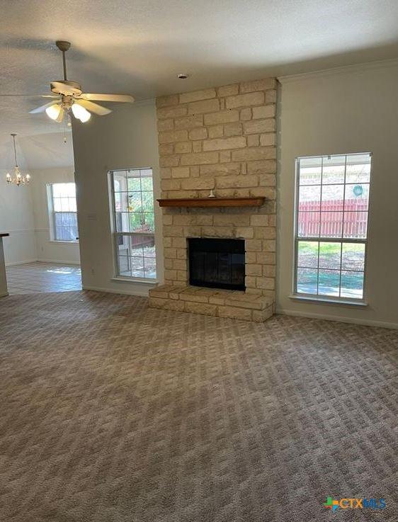 unfurnished living room featuring carpet floors, ceiling fan, crown molding, a brick fireplace, and a textured ceiling