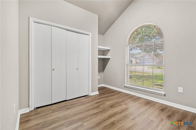 unfurnished bedroom with a closet, light hardwood / wood-style flooring, and lofted ceiling