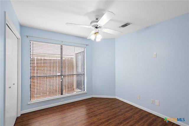 spare room featuring baseboards, visible vents, ceiling fan, and dark wood-style flooring