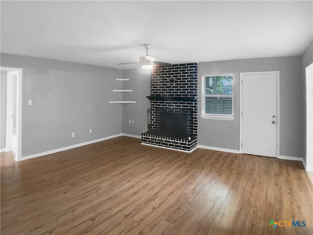 unfurnished living room featuring baseboards, a ceiling fan, wood finished floors, and a fireplace