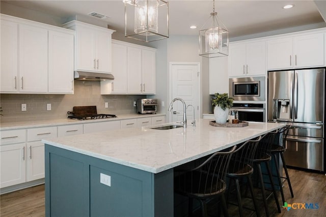 110 Terra Vista Ranch Rd, Victoria, TX 77904 - kitchen featuring appliances with stainless steel finishes, a kitchen island with sink, dark wood-style flooring, backsplash, and white cabinetry