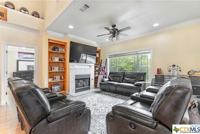 living room with light hardwood / wood-style floors, built in shelves, ceiling fan, a fireplace, and crown molding