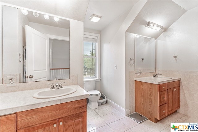 bathroom with toilet, vanity, tile patterned floors, and tile walls