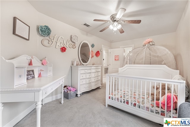 bedroom featuring a crib, light colored carpet, and ceiling fan