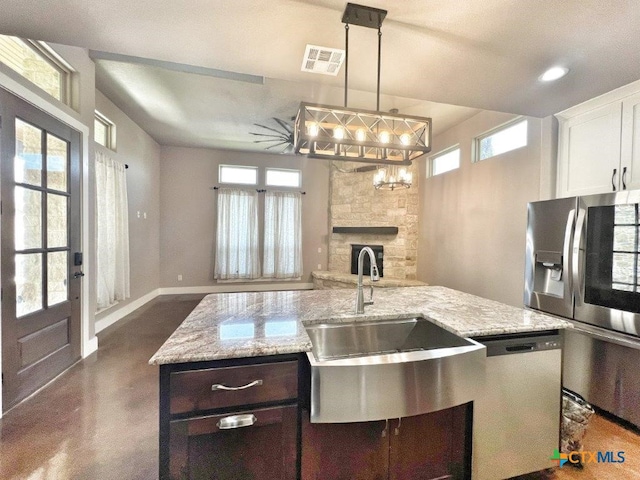 kitchen featuring a stone fireplace, dishwasher, white cabinets, sink, and pendant lighting