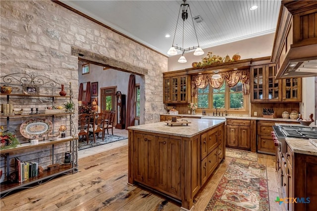 kitchen with sink, light hardwood / wood-style floors, decorative light fixtures, a kitchen island with sink, and ornamental molding