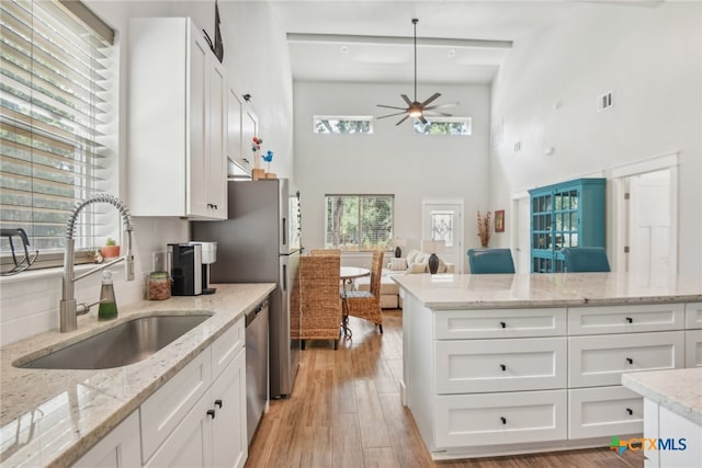 kitchen with light hardwood / wood-style floors, light stone counters, a towering ceiling, sink, and white cabinetry