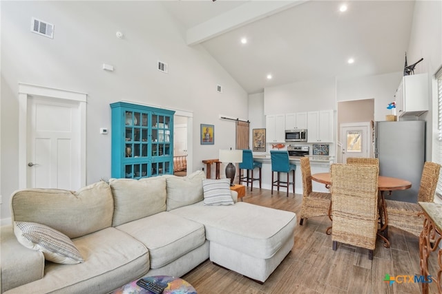 living room featuring high vaulted ceiling, a barn door, light wood-type flooring, and beam ceiling