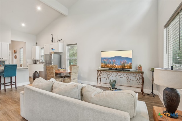 living room with a healthy amount of sunlight, light hardwood / wood-style flooring, high vaulted ceiling, and beam ceiling