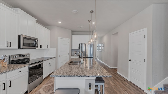 kitchen featuring light hardwood / wood-style flooring, sink, an island with sink, pendant lighting, and appliances with stainless steel finishes