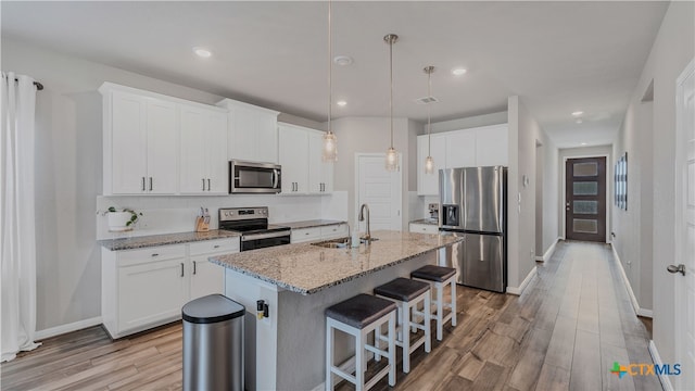 kitchen featuring white cabinetry, a kitchen island with sink, light stone counters, and stainless steel appliances