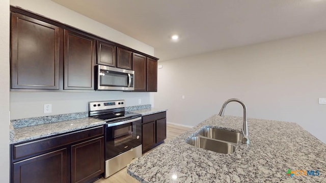 kitchen with light stone countertops, appliances with stainless steel finishes, sink, and dark brown cabinets