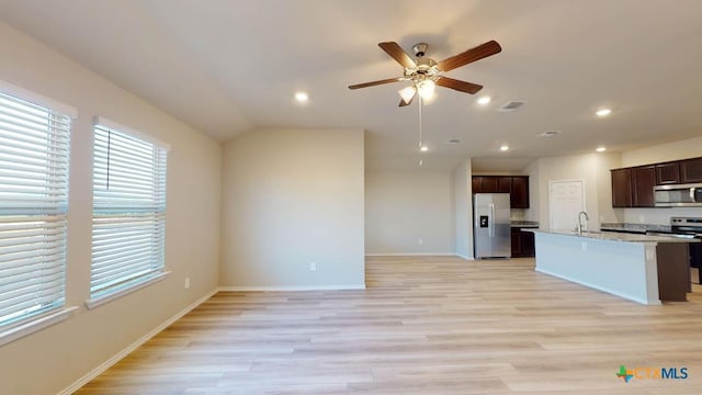 kitchen with lofted ceiling, sink, light stone counters, stainless steel appliances, and light hardwood / wood-style floors