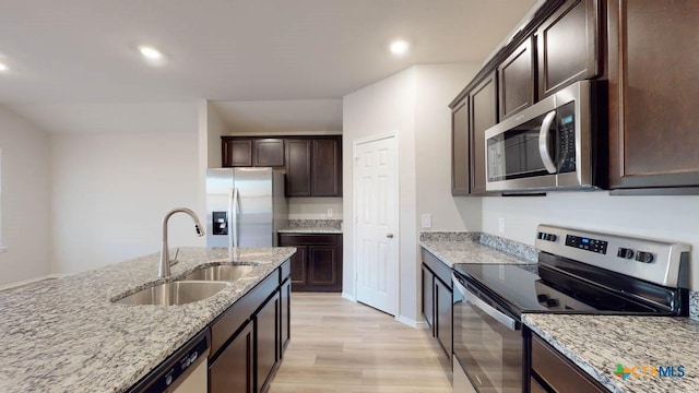 kitchen with sink, dark brown cabinets, light wood-type flooring, stainless steel appliances, and light stone countertops