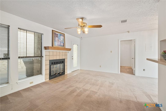 unfurnished living room with light carpet, visible vents, a tiled fireplace, ceiling fan, and a textured ceiling